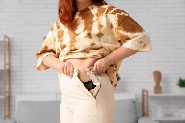 Image of woman trying to do her trousers up after pregnancy weight gain Thames Ditton